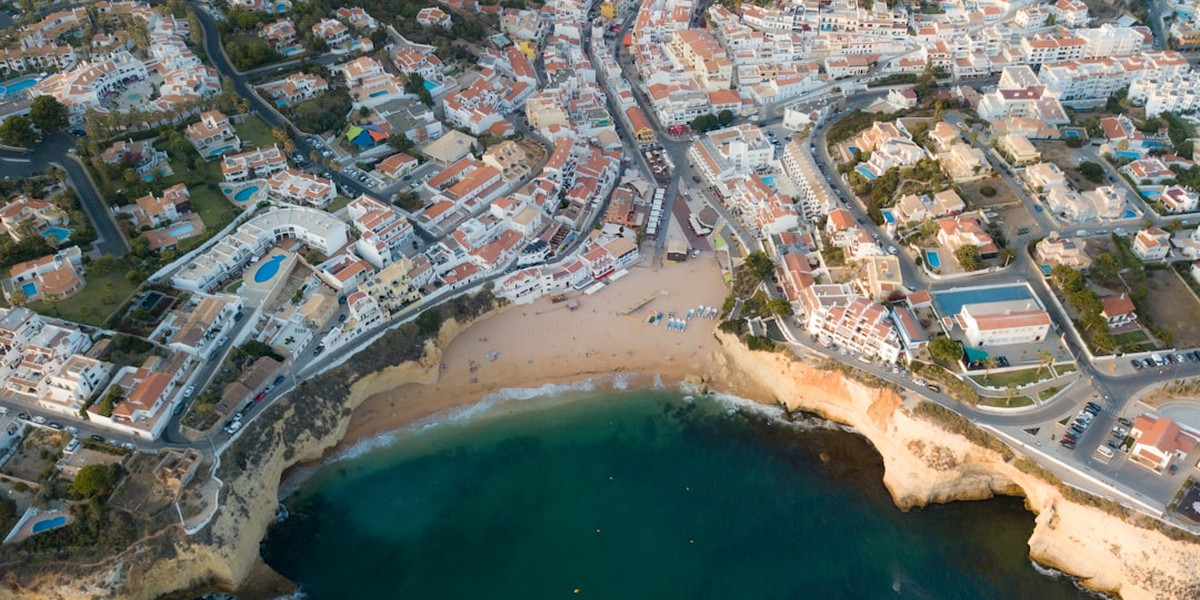 Aerial view of Algarve beach town with golden cliffs, sandy cove and white buildings with terracotta roofs