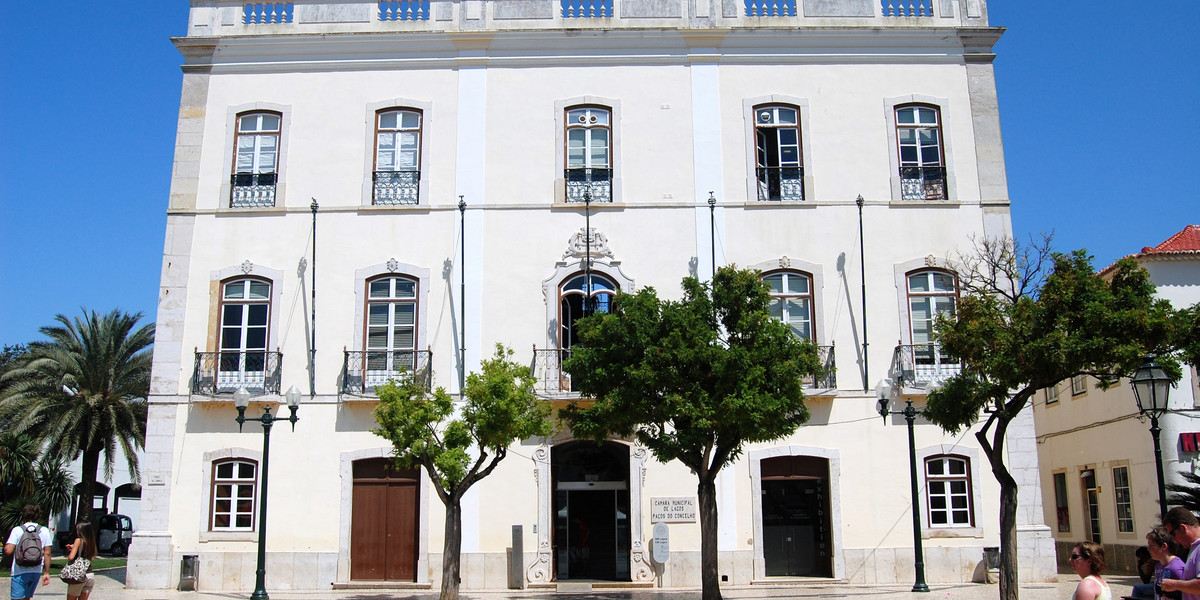 Historic white Portuguese colonial building with arched windows in sunny town square with palm trees