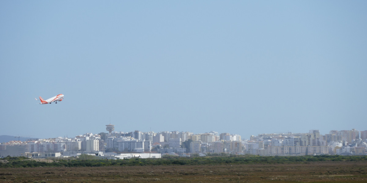 Commercial airplane taking off over Algarve coastal city with marshlands in foreground