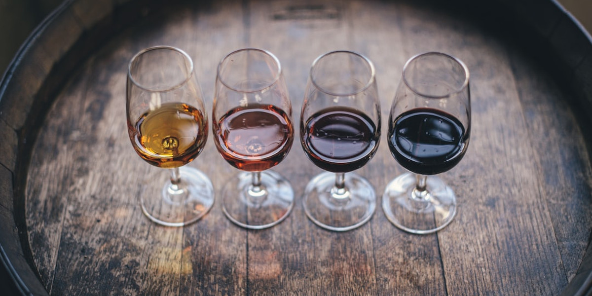 Four wine glasses with different colored wines arranged on wooden barrel for tasting