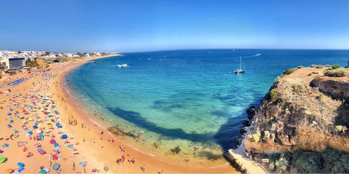 Aerial view of crowded Algarve beach with golden cliffs, turquoise water, and colorful umbrellas