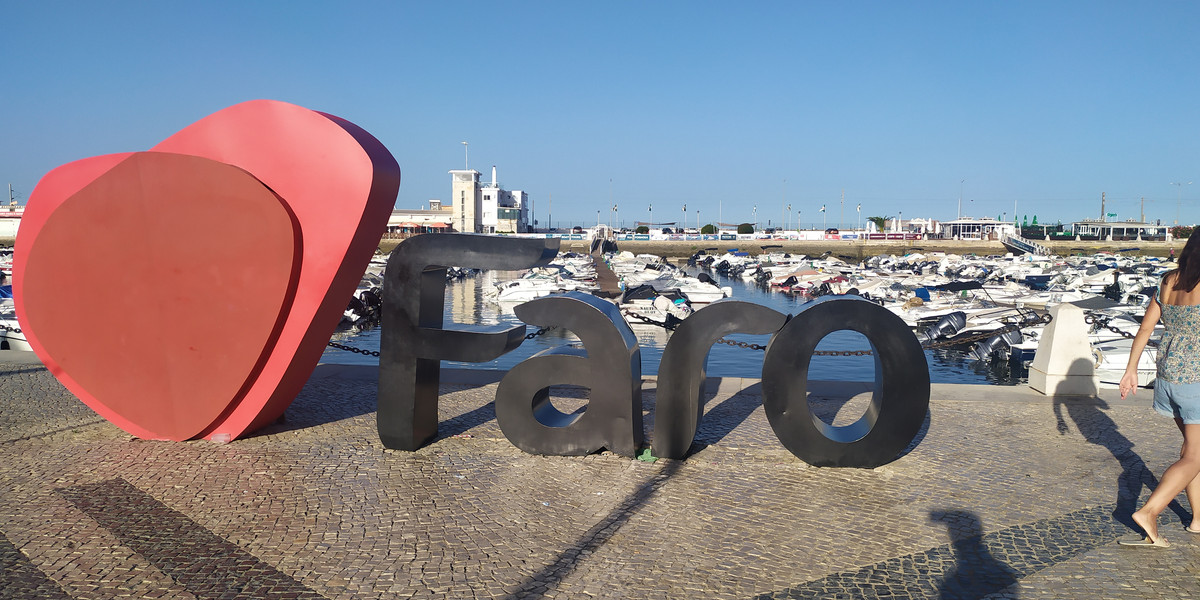 Pink heart and Faro text sculpture on waterfront promenade with marina view