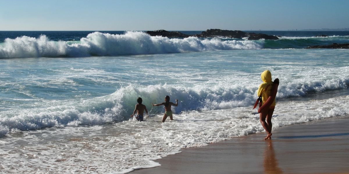 People playing in large ocean waves on an Algarve beach with dramatic surf and rocky outcrops