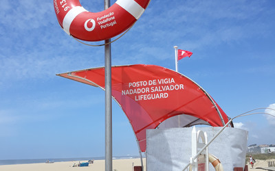 Red and white lifeguard station with rescue equipment on Portuguese beach under blue sky